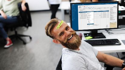 Mann mit Bart vor PC Bildschirm mit Aufkleber auf Stirn